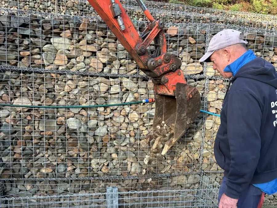 Gabion baskets being filled with rock to form a retaining wall