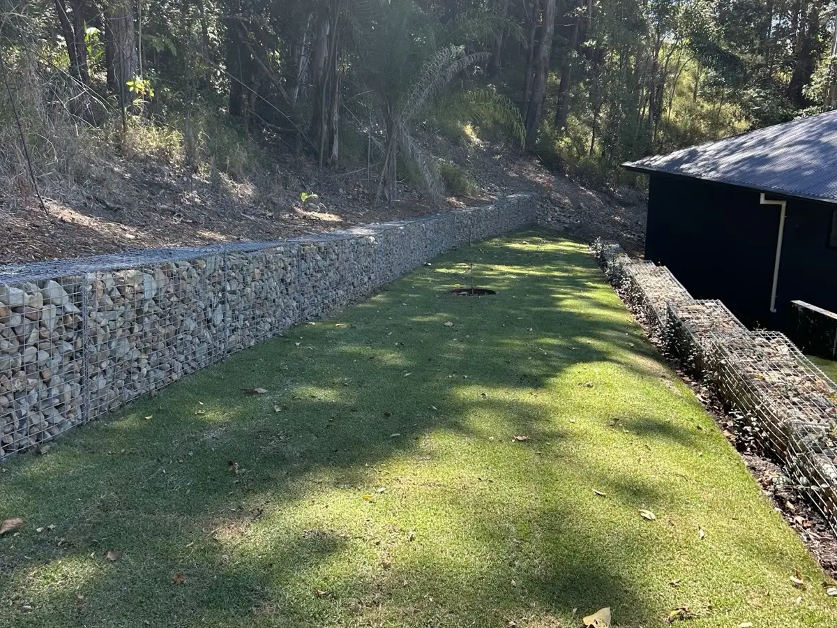 Gabion retaining wall running the length of a rear yard with newly laid turf